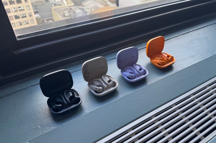 Four open Beats Powerbeats Pro 2 cases in Jet Black, Quick Sand, Hyper Purple, Electric Orange on a window sill.