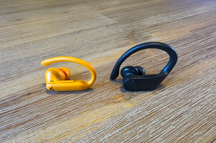 A Beats Powerbeats Pro 2 earbud next to a Powerbeats Pro earbud on a wooden floor.