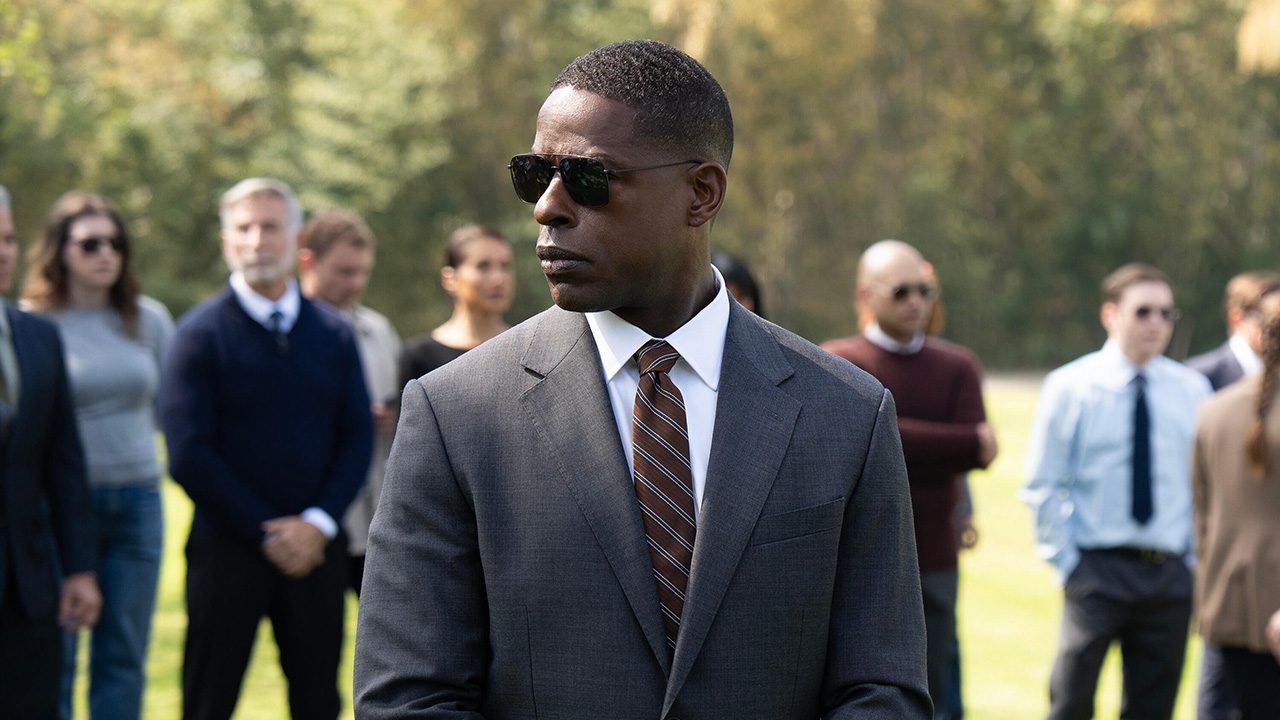Sterling K. Brown wearing sunglasses and a suit standing outside with people behind him in Paradise.