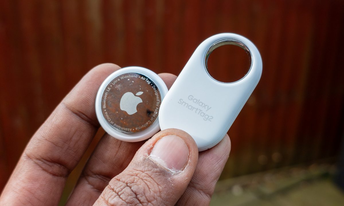 Apple AirTag and Samsung Galaxy Tag 2 held together in the palm of a hand