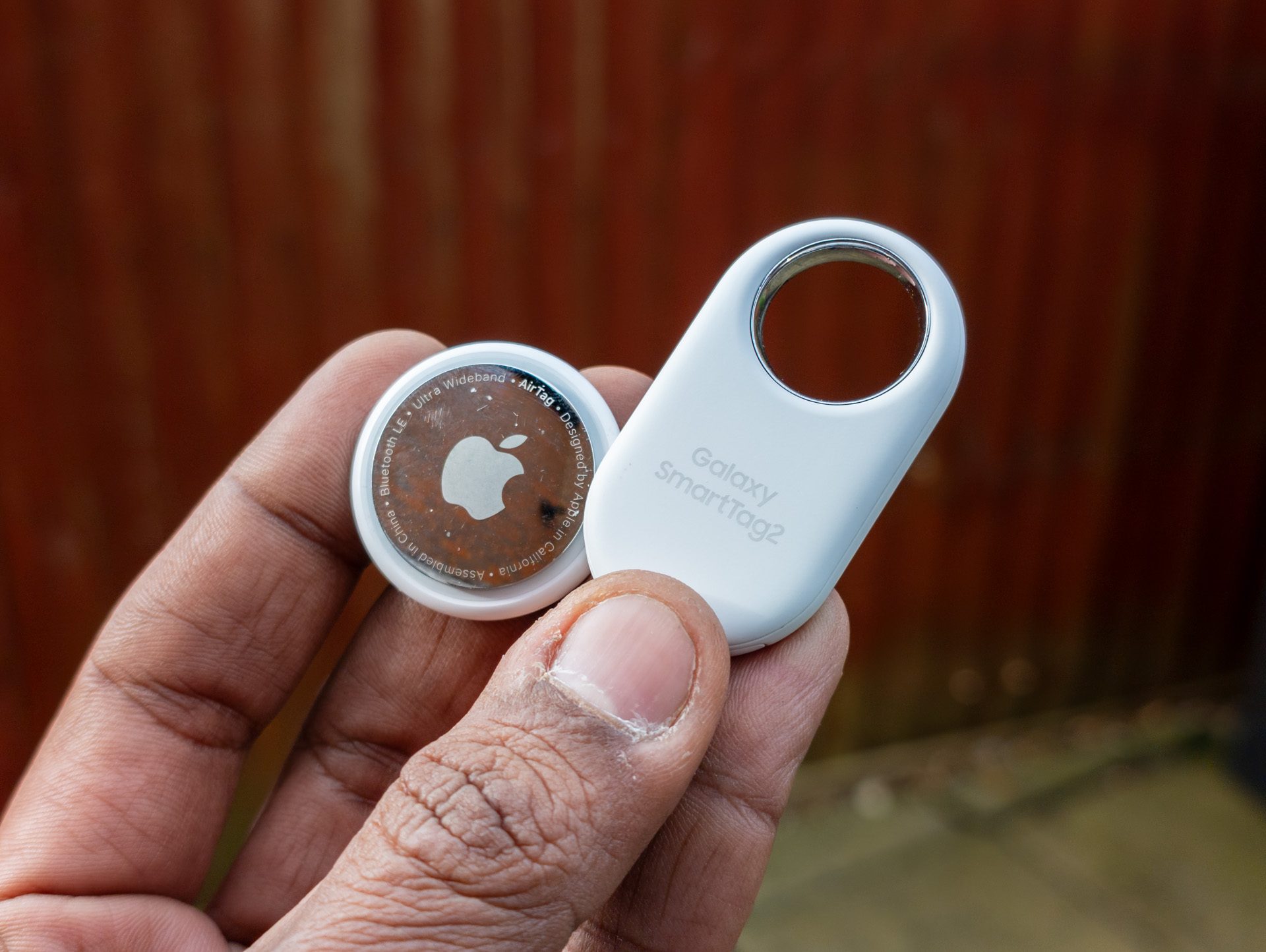 Apple AirTag and Samsung Galaxy Tag 2 held together in the palm of a hand
