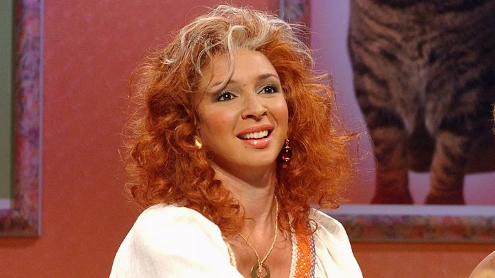 Maya Rudolph with an orange and blonde wig smiling on SNL.