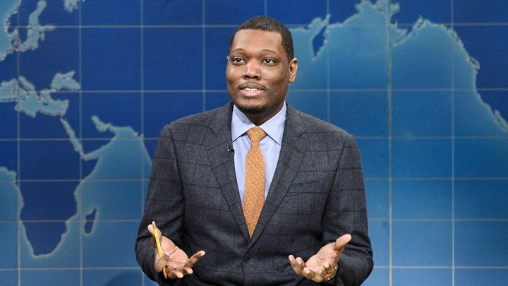Michael Che on Weekend Update on SNL with his hands out turned while talking.