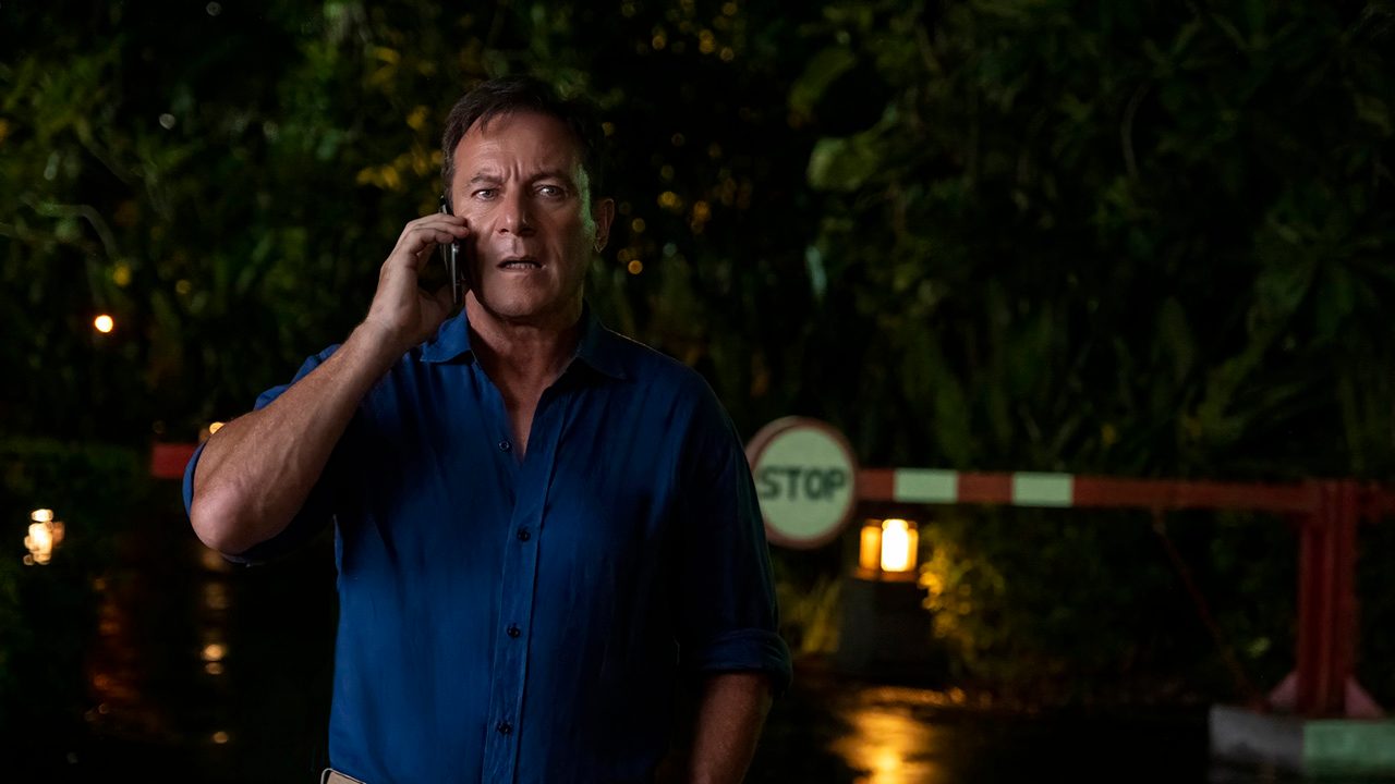 Jason Isaacs in a blue shirt on the phone outside in The White Lotus season 3.