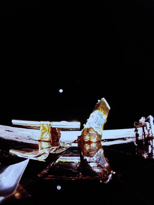 This image shows the Moon's surface, Earth on the horizon, and Blue Ghost's top deck with its solar panel, X-band antenna (left), and LEXI payload (right) in the view.