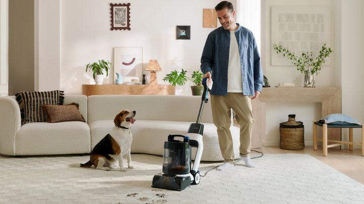 man using carpet cleaner while pet looks at him
