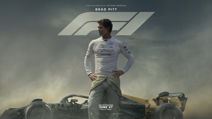 Brad Pitt has his hands at his hips in front of a car.