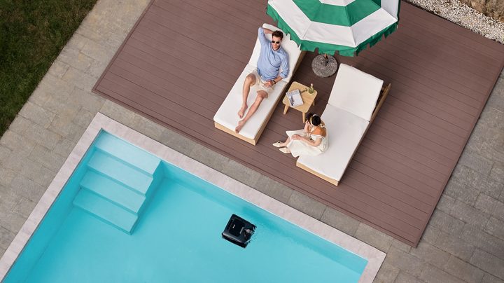 Man sitting by pool with a robot pool cleaner