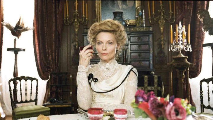 Michelle Pfeiffer as Léa de Lonval at a dinner table holding a glass in Chéri.