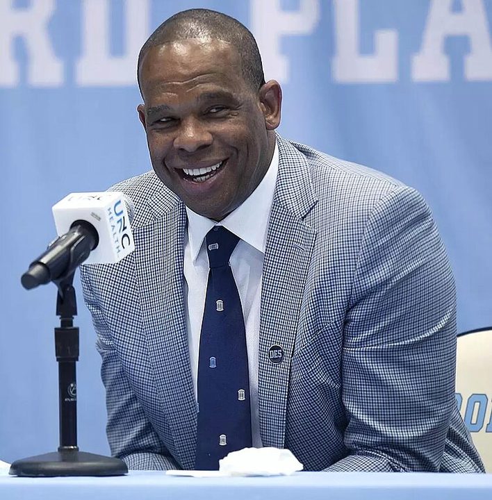 A man smiles while speaking at a mic.