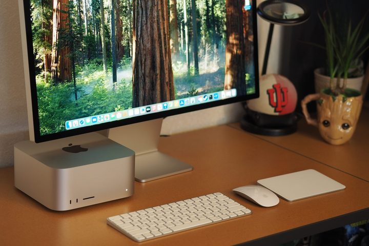 Apple Mac Studio 2025 front view showing desktop, monitor, keyboard, mouse, and touchpad.