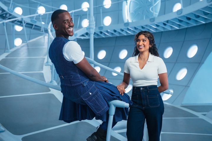 Doctor Who sits on a rail with Belinda next to him.