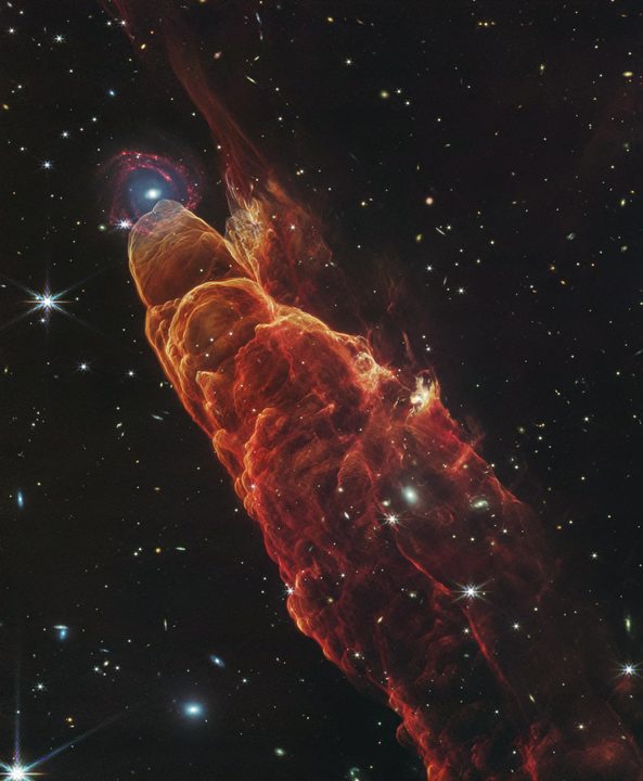 The NASA/ESA/CSA James Webb Space Telescope observed Herbig-Haro 49/50, an outflow from a nearby still-forming star, in high-resolution near- and mid-infrared light with the NIRCam and MIRI instruments. The intricate features of the outflow, represented in reddish-orange color, provide detailed clues about how young stars form and how their jet activity affects the environment around them. A chance in this direction of the sky provides a beautiful juxtaposition of this nearby Herbig-Haro object (located within our Milky Way) with a more distant, face-on spiral galaxy in the background.