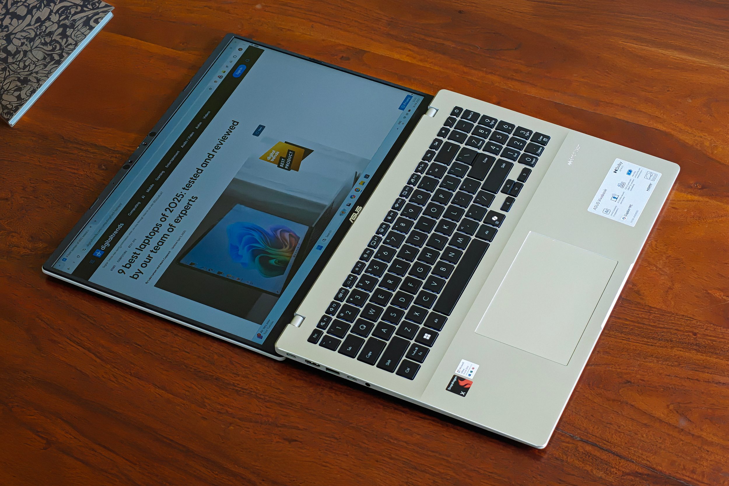 Display on the Asus Vivobook 16 X1607QA Copilot+ PC laptop with Qualcomm Snapdragon X ARM 64 chip lays out 180-degrees on a wooden surface.