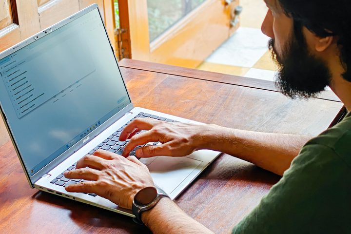 Man typing on the Asus Vivobook 16 X1607QA Copilot+ PC laptop with Qualcomm Snapdragon X ARM 64 chip kept on on a wooden surface.