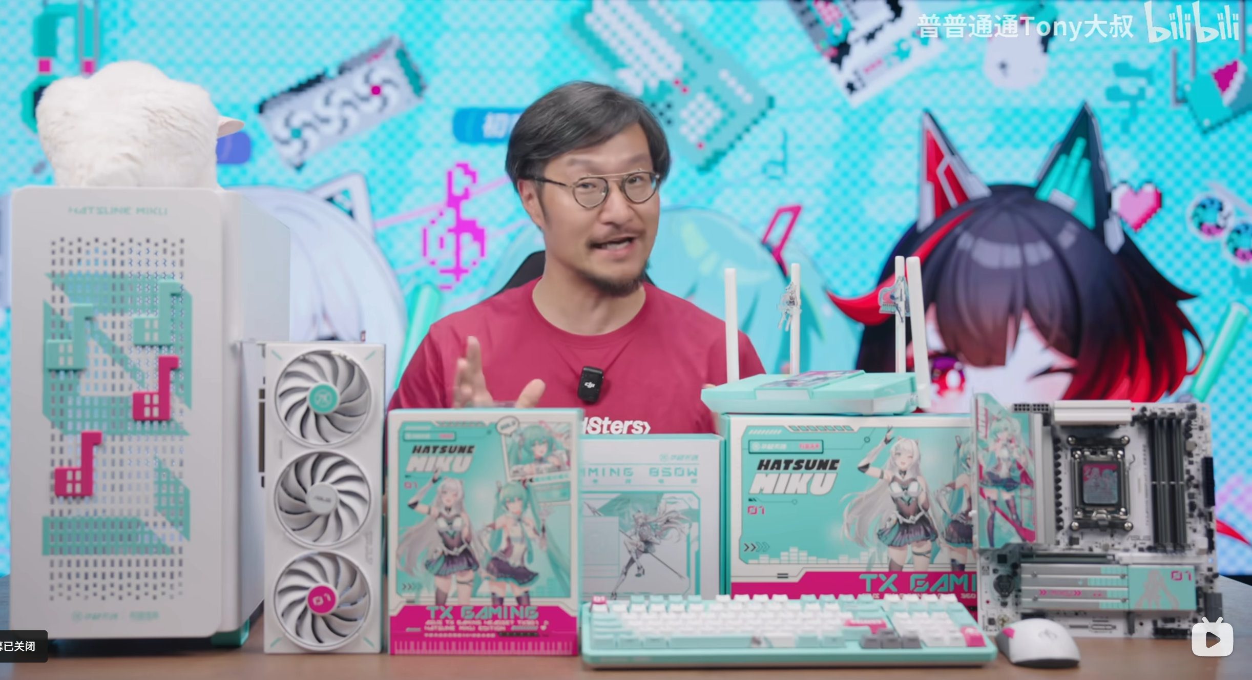 A man sits behind a table with a lot of Asus x Hatsune Miku hardware on it.