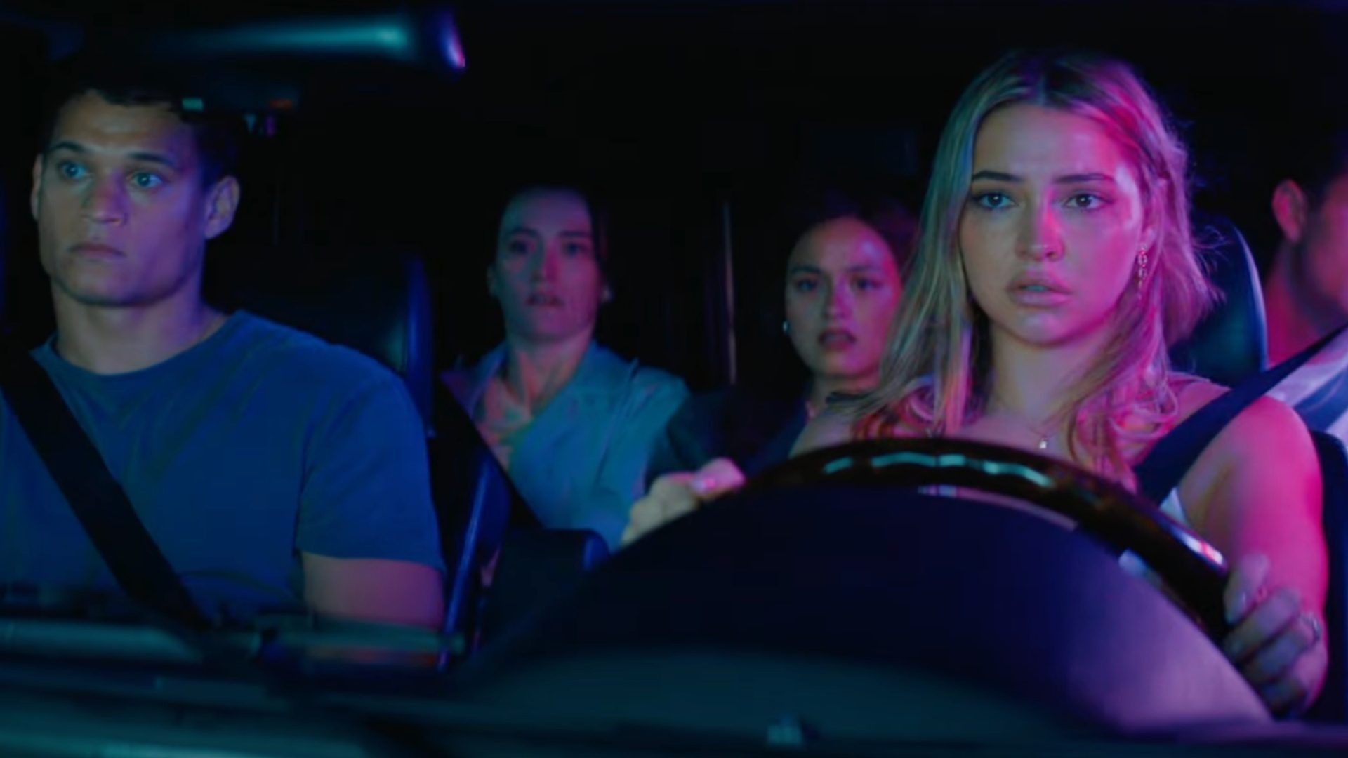 A group of teens sit in a car and look scared.