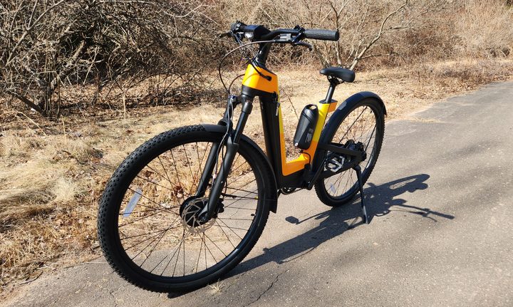 Urtopia Fusion GT e-bike parked on pavement left front three-quarter view with trees and brush in the background.
