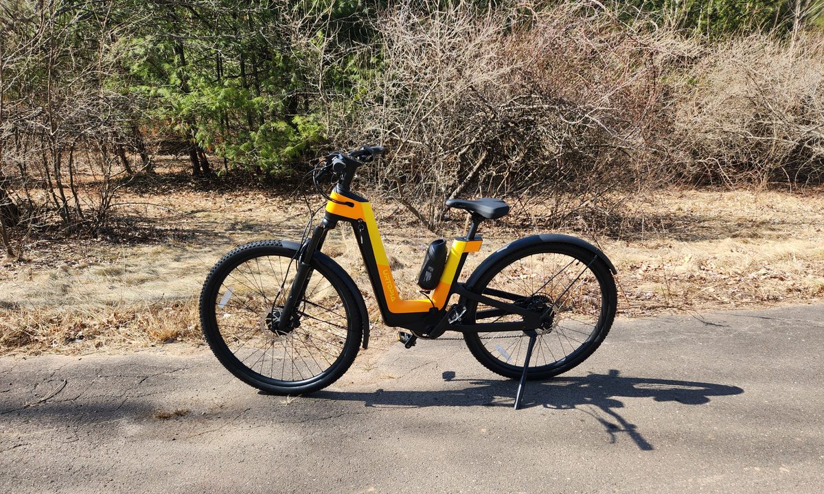 Urtopia Carbon Fusion GT e-bike parked on pavement left profile view with trees and brush in the background.