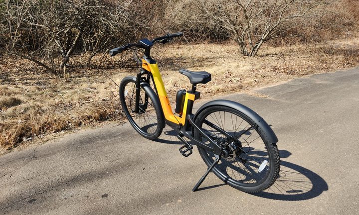 Urtopia Carbon Fusion GT e-bike parked on pavement left rear three-quarter view with trees and brush in the background.