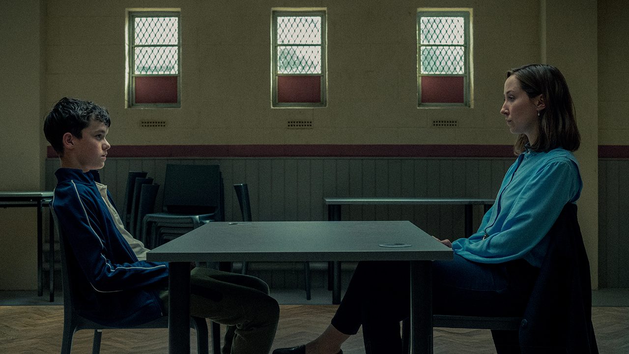 A young boy sits across from a woman in a dark room in Adolescence.