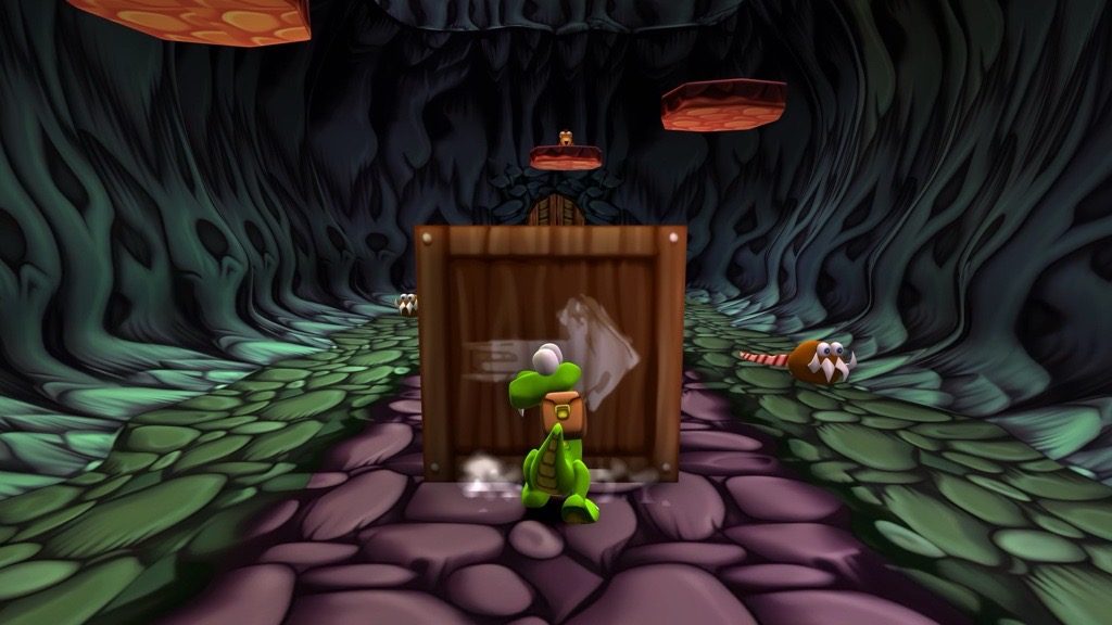 Croc pushes a box forward inside a cave in Croc: Legend of the Gobbos Remastered.