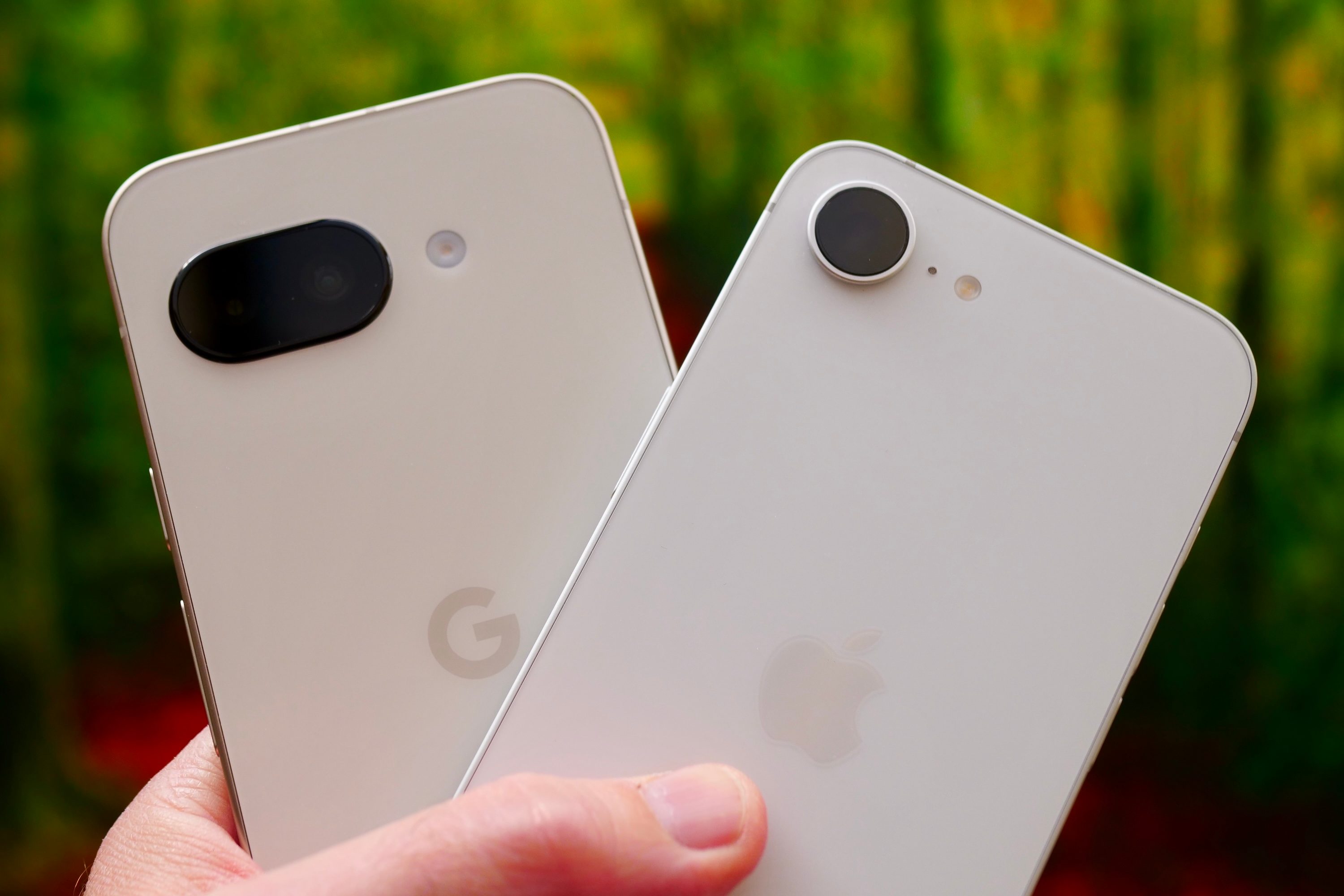 A person holding the Google Pixel 9a and Apple iPhone 16e.