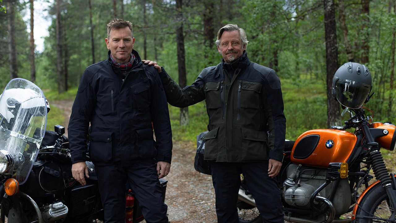 Two men pose beside their motorcycles in Long Way Home on Apple TV+.
