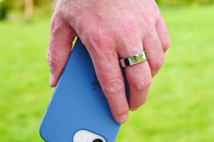 A person wearing the Noise Luna Ring and holding an Apple iPhone 16E.