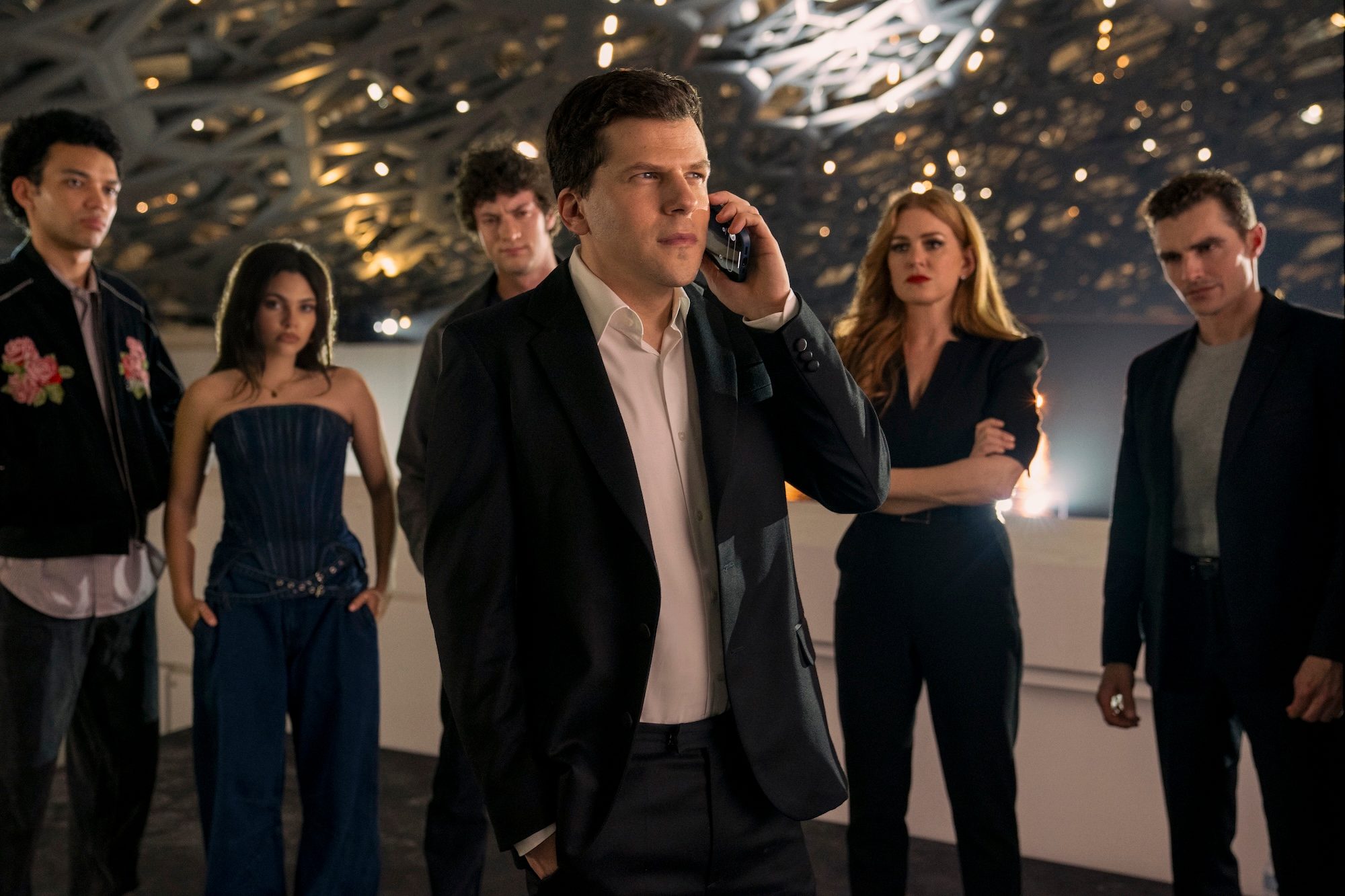 A group of magicians stand around one man on the phone.