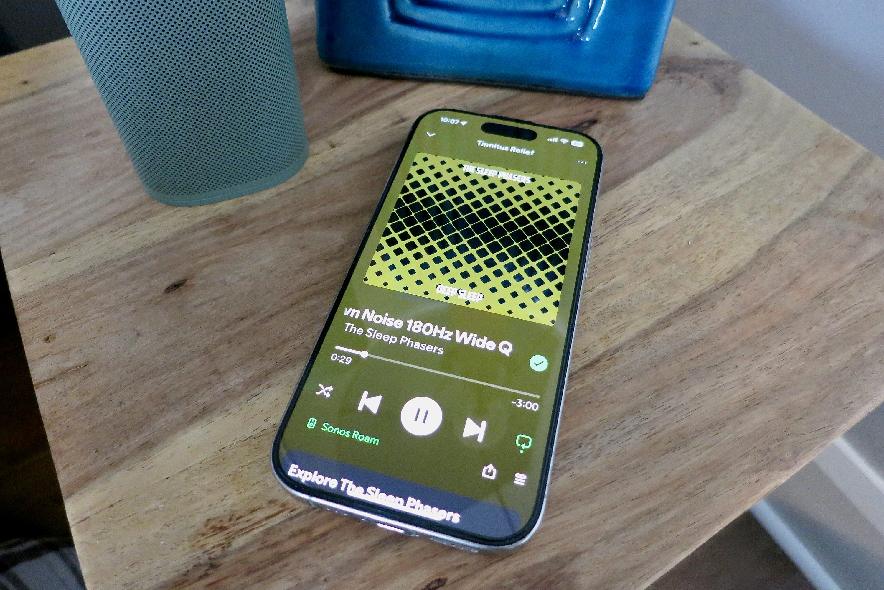 An iPhone on a bedside table with a sleep playlist on the screen.