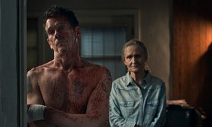 Kevin Bacon standing arms folded bloody with no shirt as a woman looks on behind him in The Bondsman.