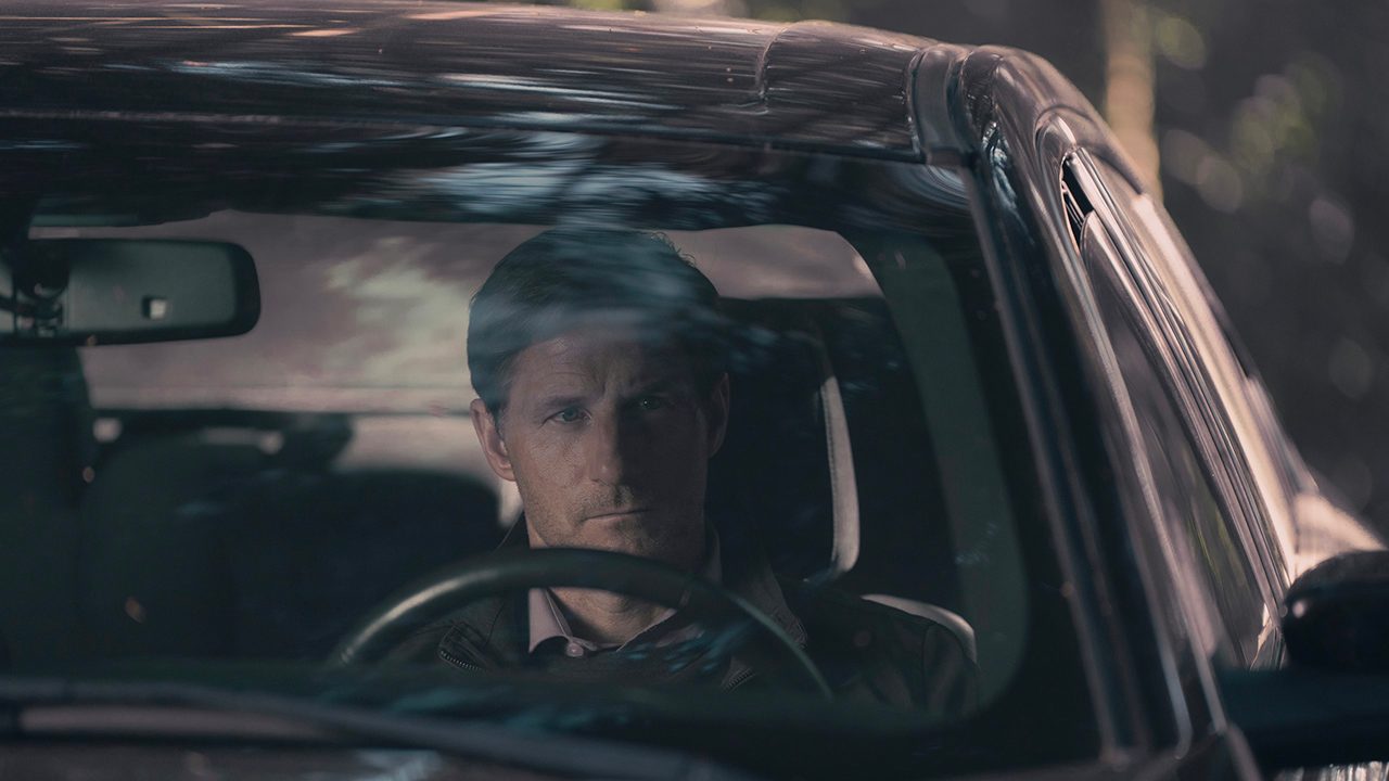 Mark Tuello sitting in the driver's sear of his car scoping out something in The Handmaid's Tale.
