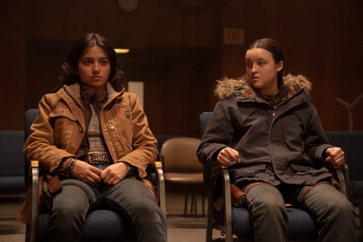Two girls sit in chairs next to one another.