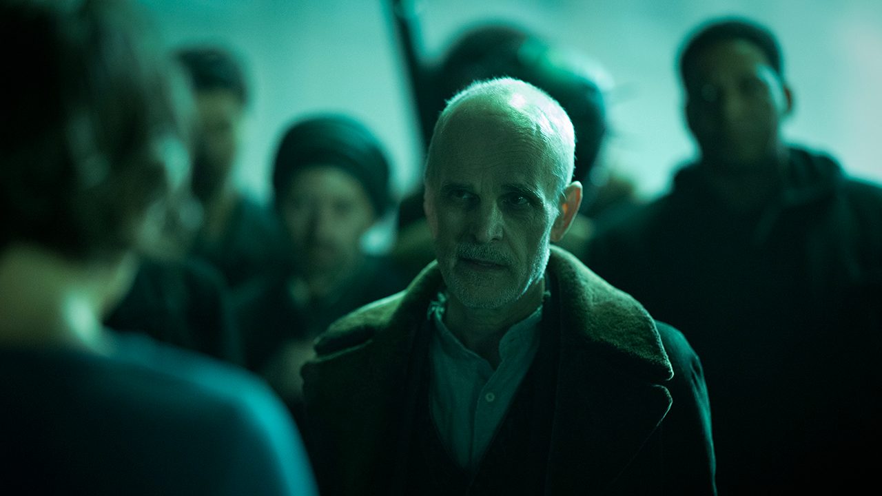 The Croat in a dark setting talking to someone with people behind him in The Walking Dead: Dead City.