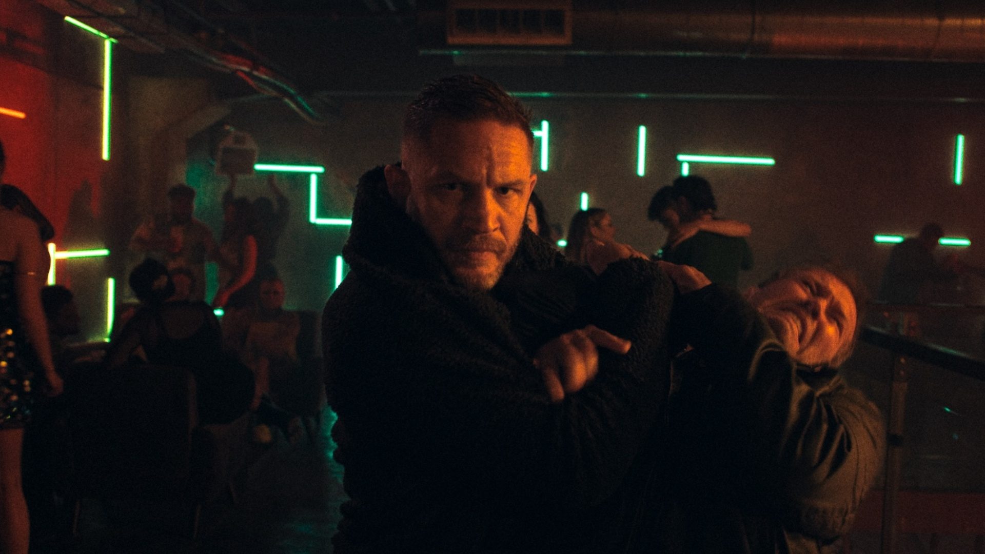 Tom Hardy points a gun and stares.