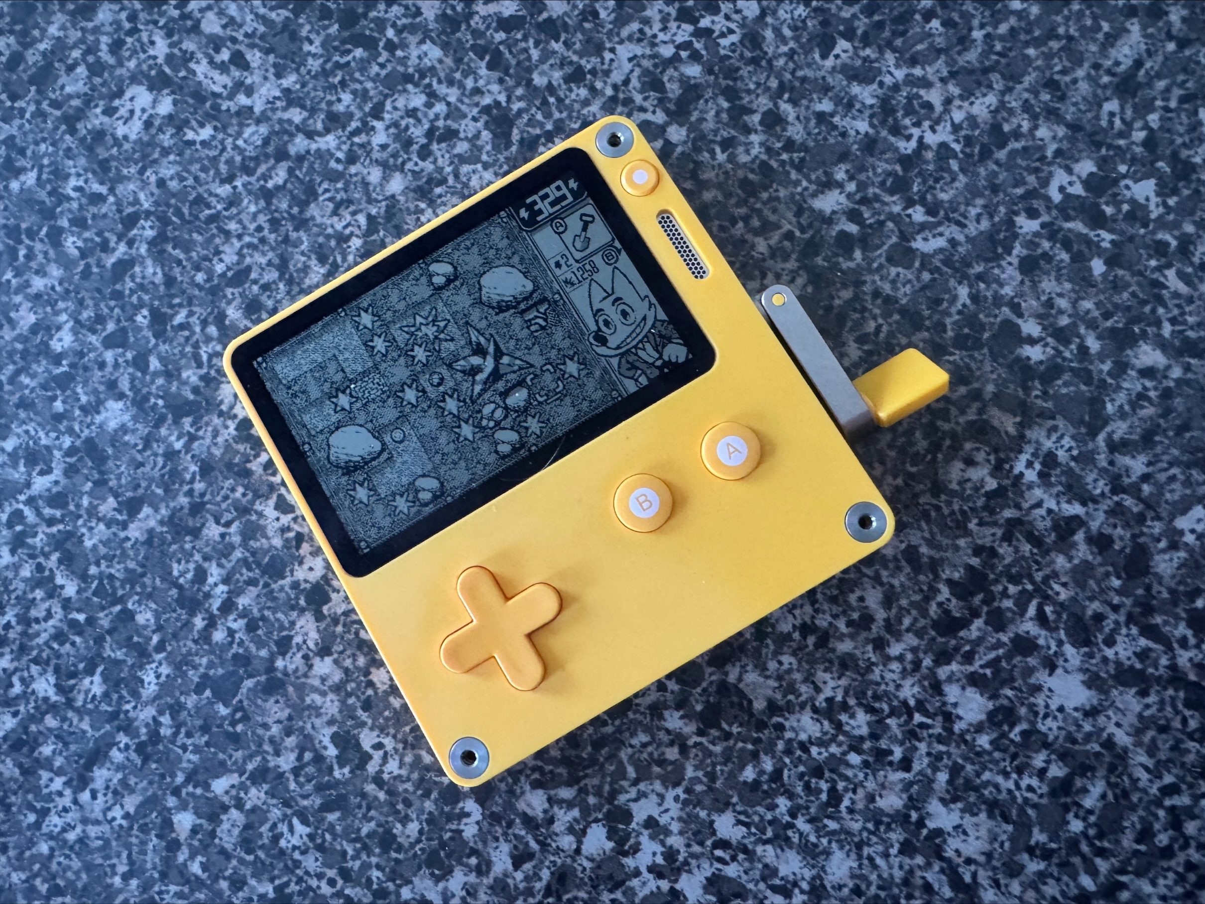 A Playdate sits on a table as Dig Dig Dino appears on screen.
