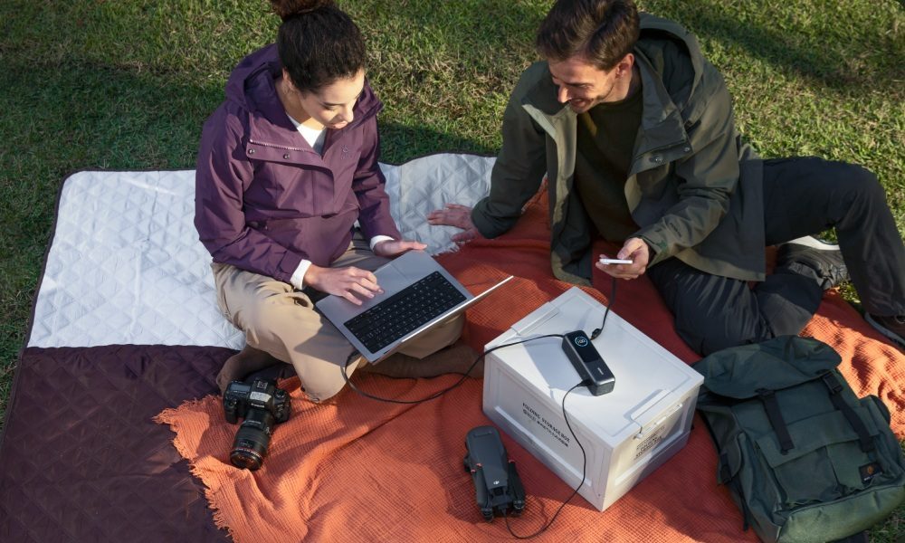 A couple have a work picnic with an Anker Power Bank and all their tech gear.