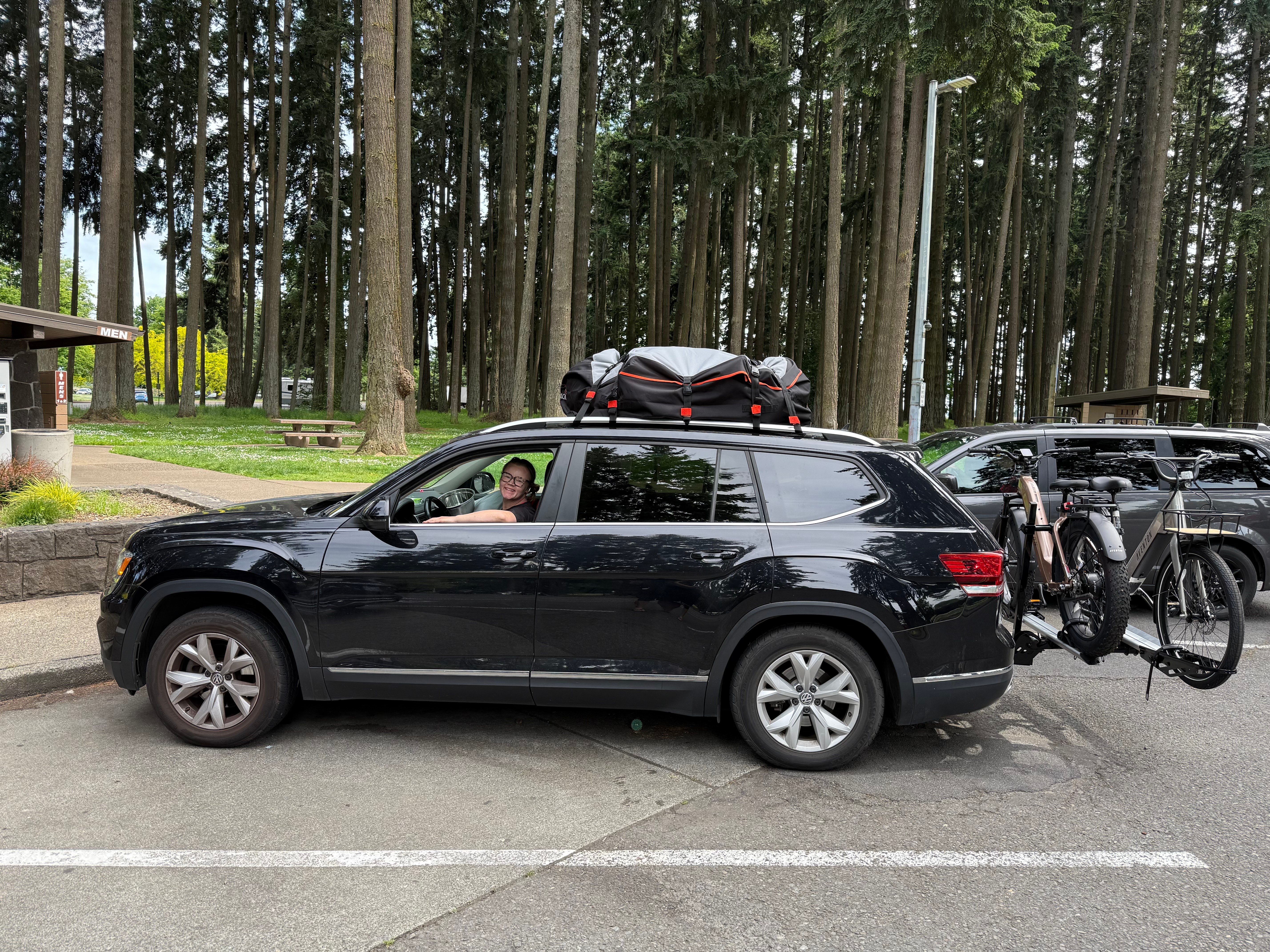 Woman sat in a black car, parked in a forest parking lot