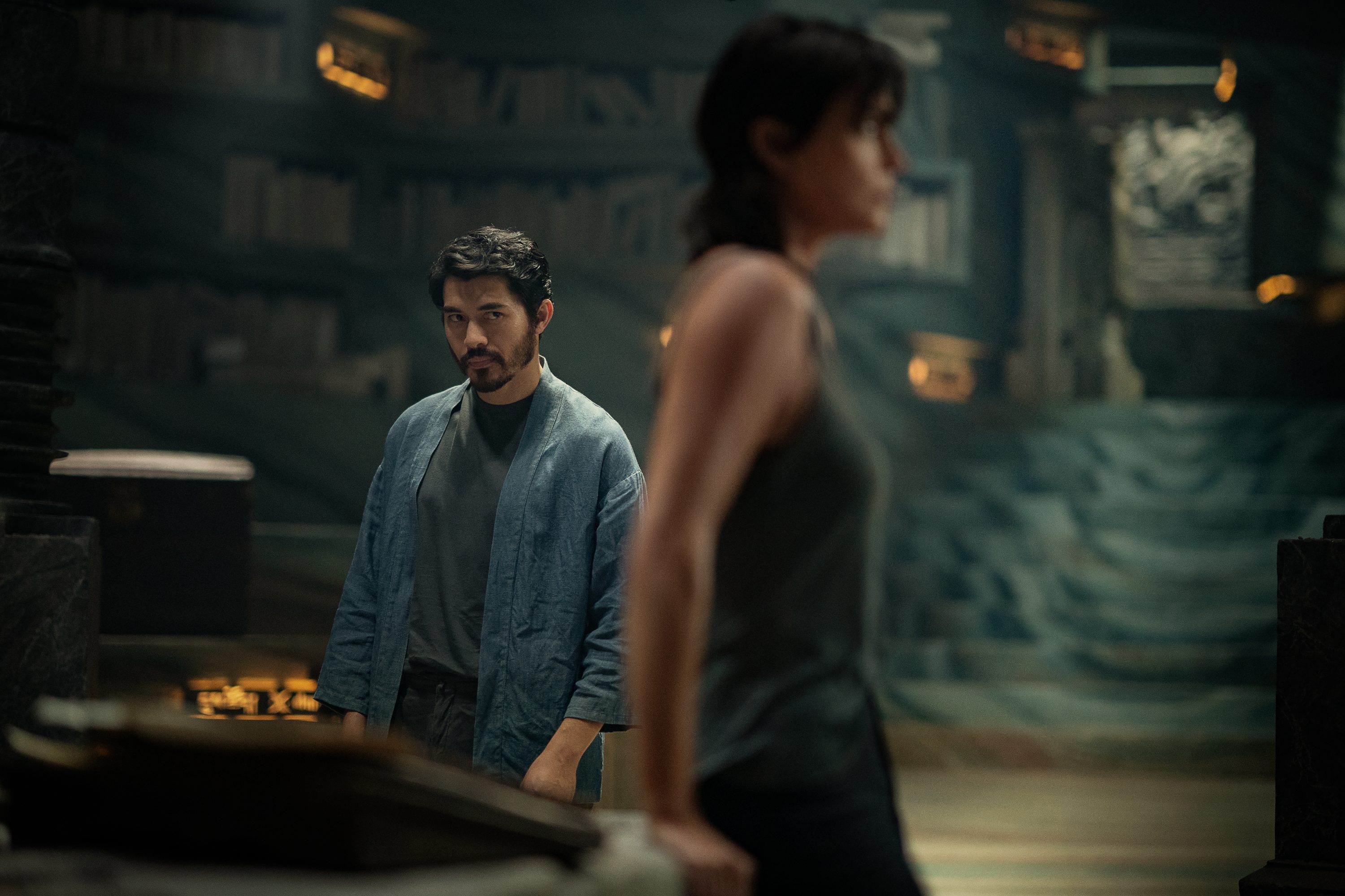 A man stands at a computer as a woman walks by.