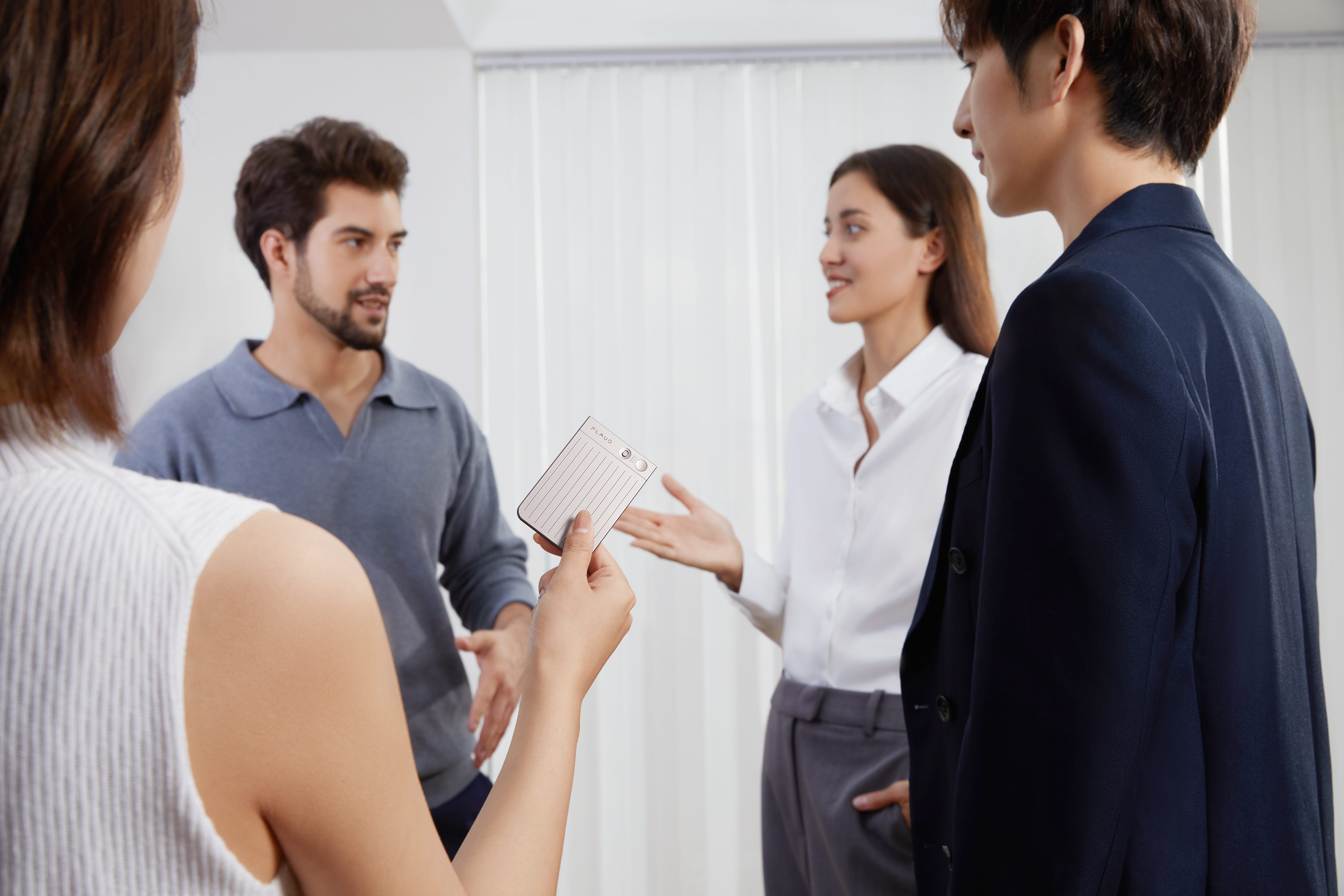 Four colleagues have a conversation around a Plaud Note AI notetaker.