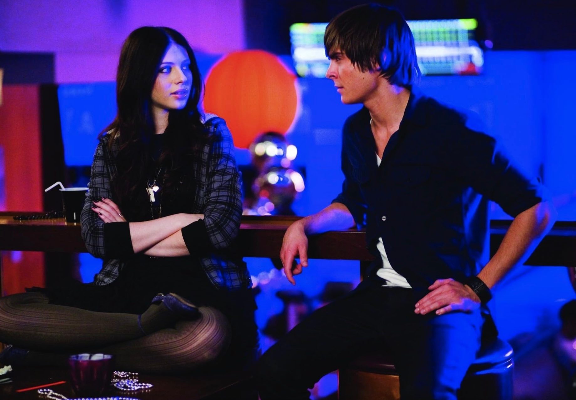 Zac Efron leans against a rail with a girl.