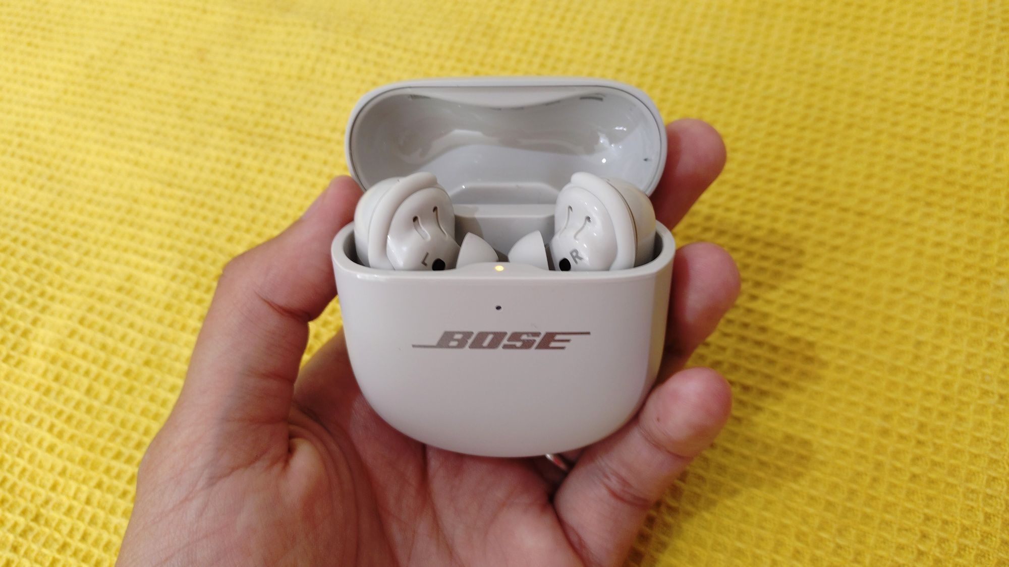Bose QC Ultra 2nd Gen in their case, being held against a yellow background