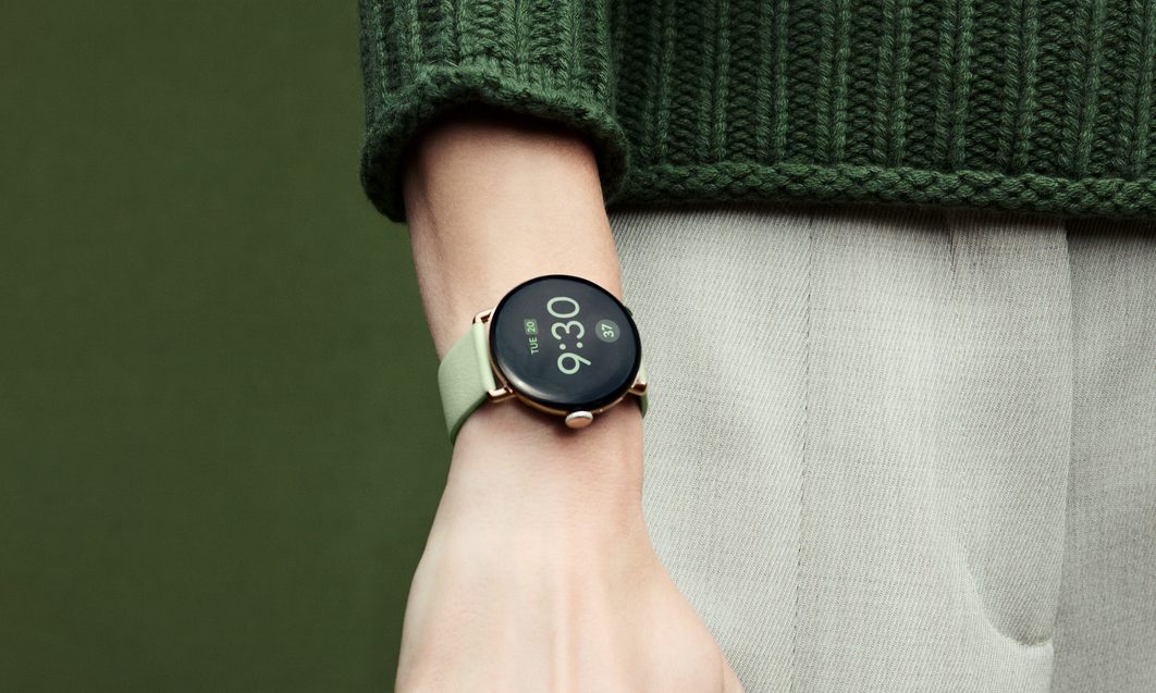 The Google Pixel Watch 4 on the wrist of a person in a green jumper.