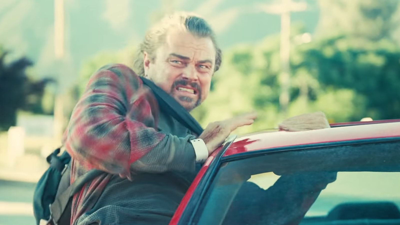 Leonardo DiCaprio poking out the window of a moving car in One Battle After Another.