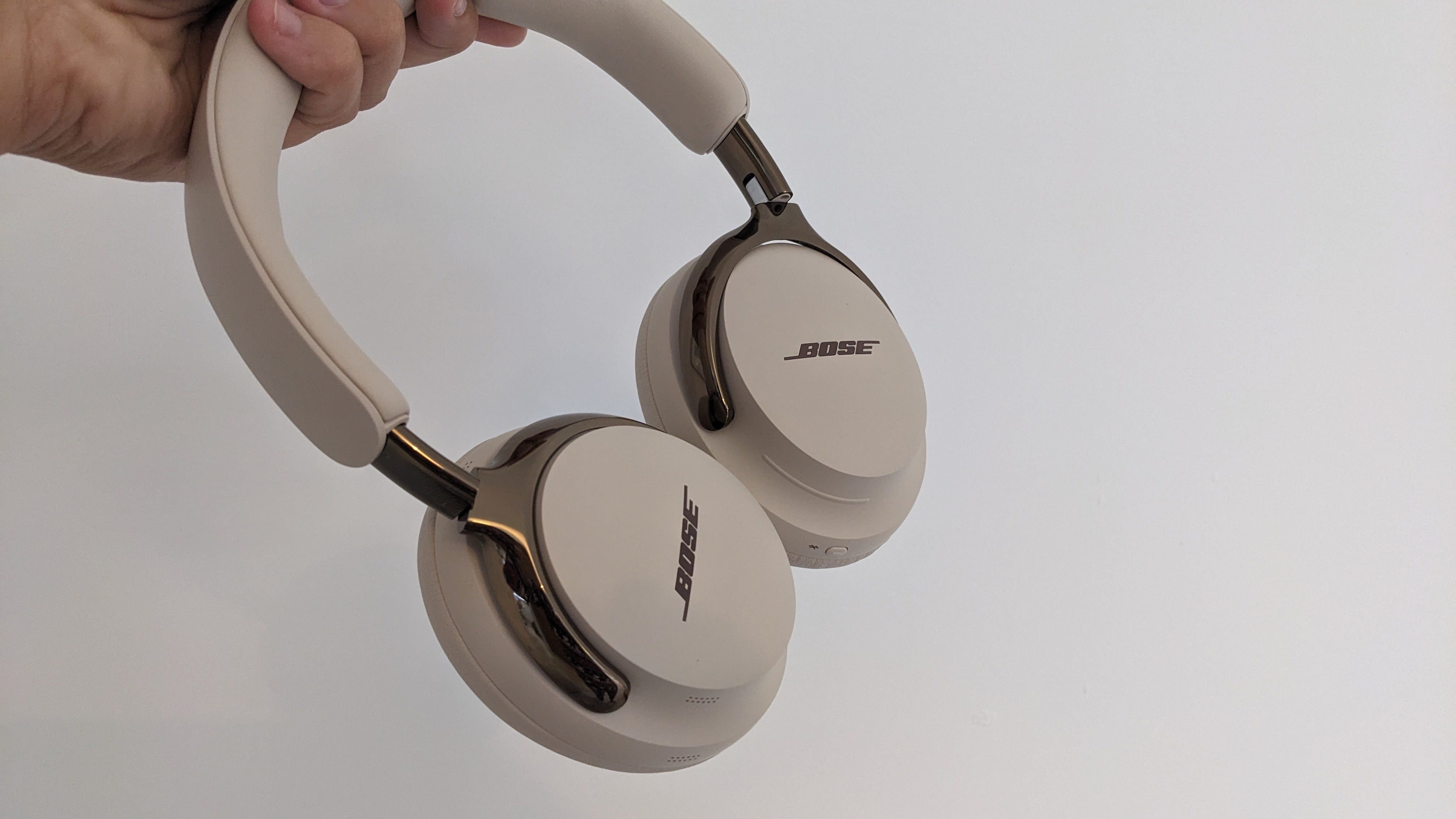 Beige Bose QuietComfort Ultra Headphones (2nd Gen) being held against a white wall