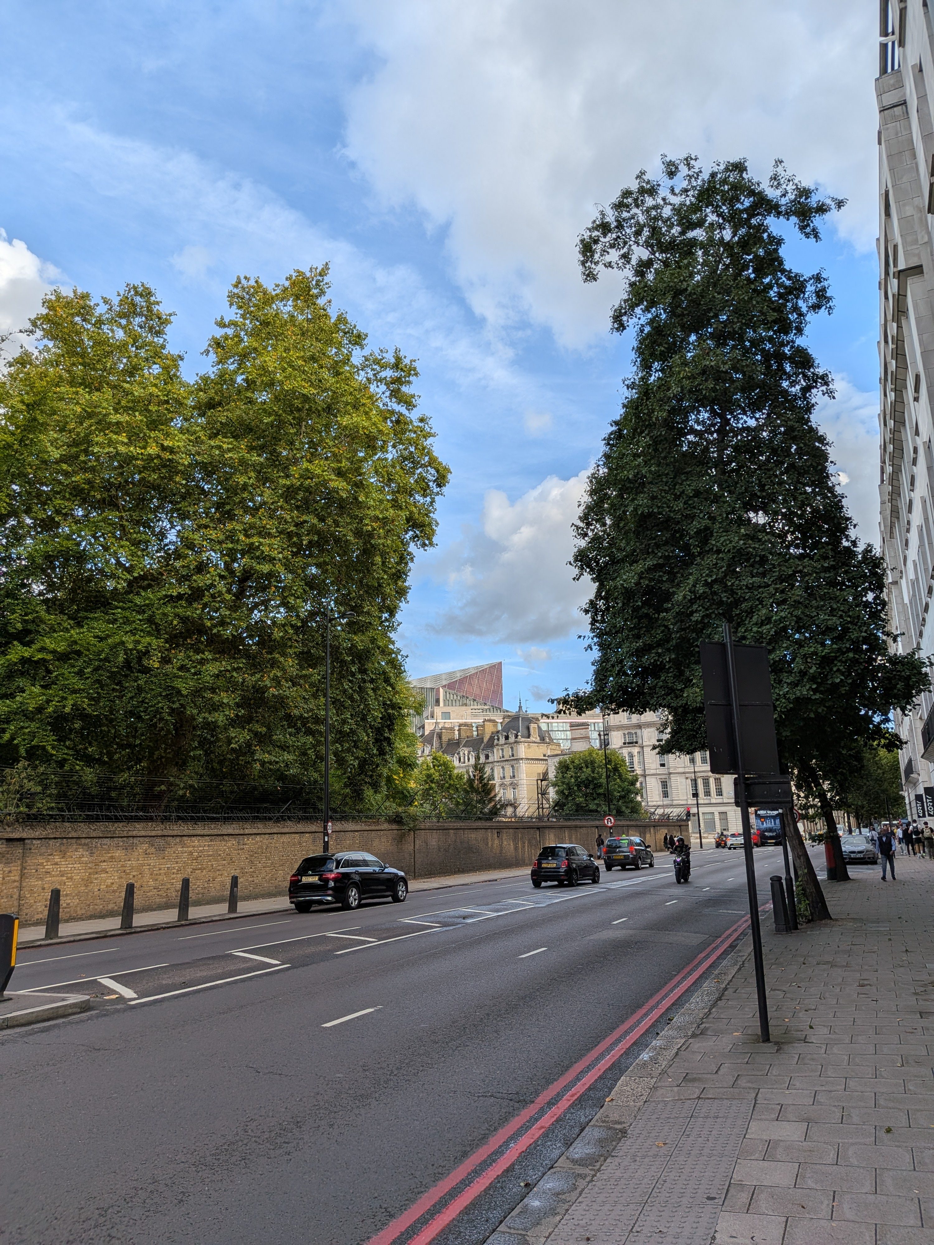 A road in London with  a pink-hued skyscraper in the distance, poking out of the skyline in London