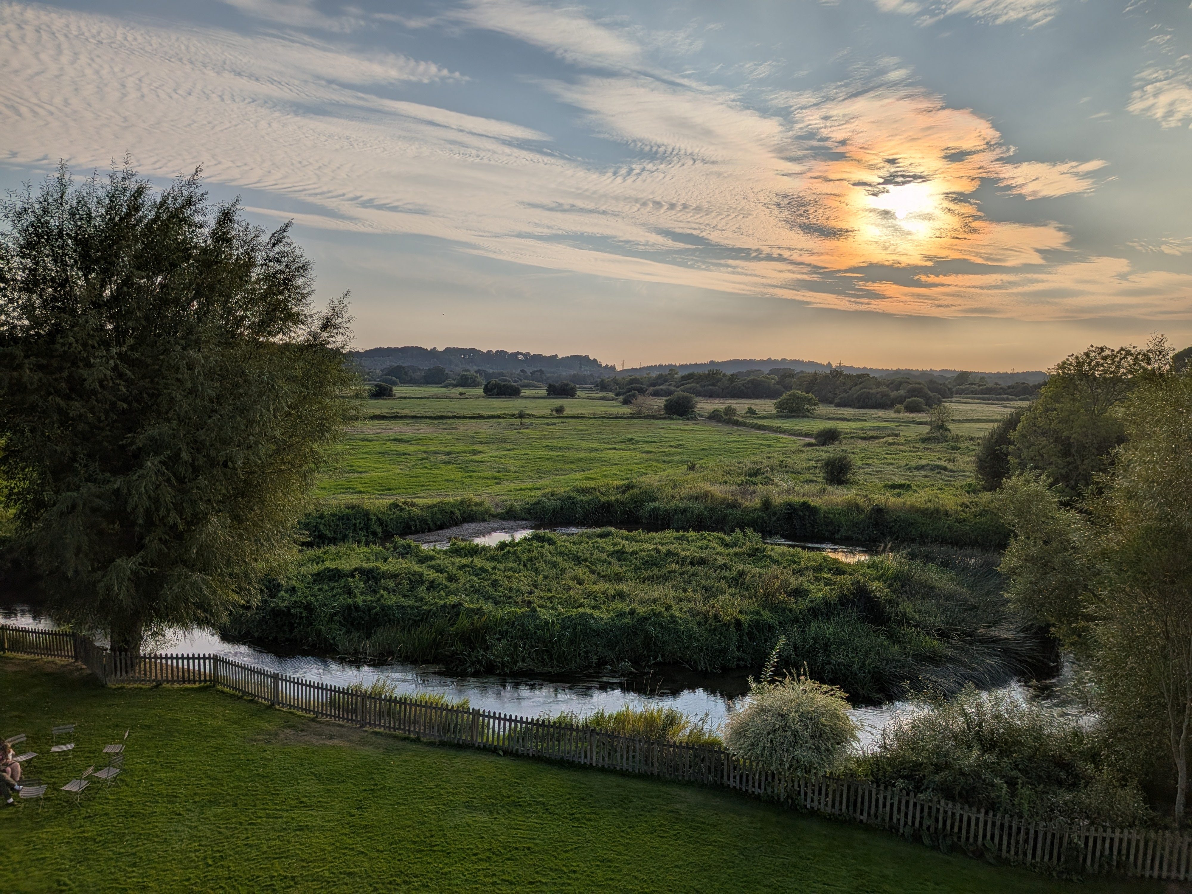 A sun setting over fields and a stream