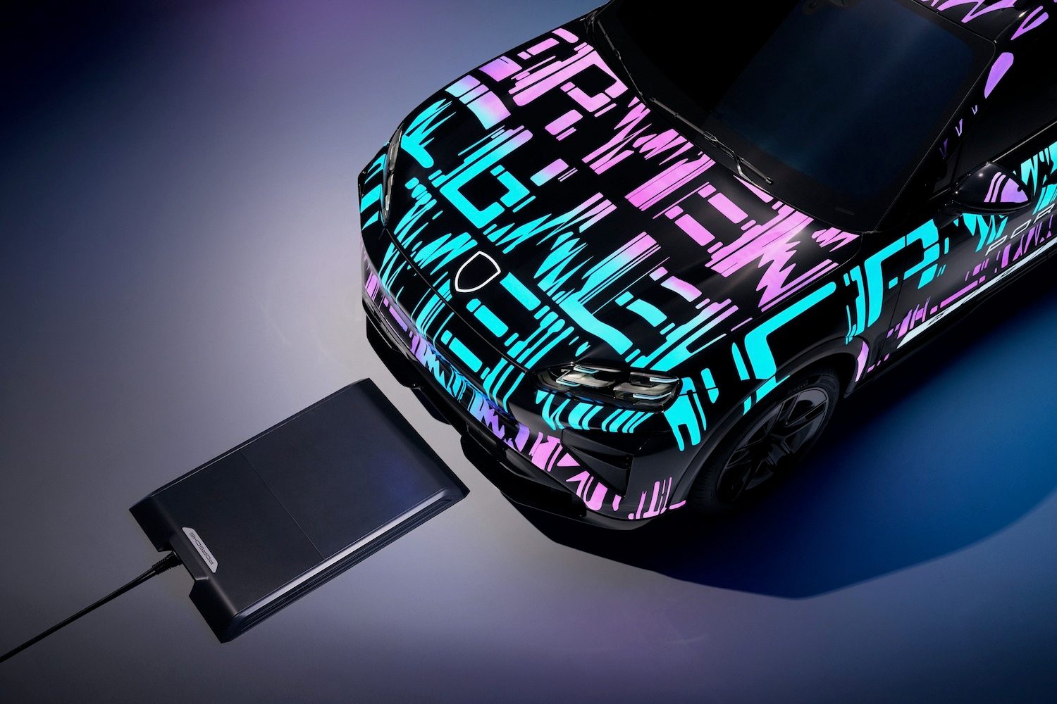 Close-up for the front of a Porsche Cayenne Electric in bright camouflage and a wireless charging pad.