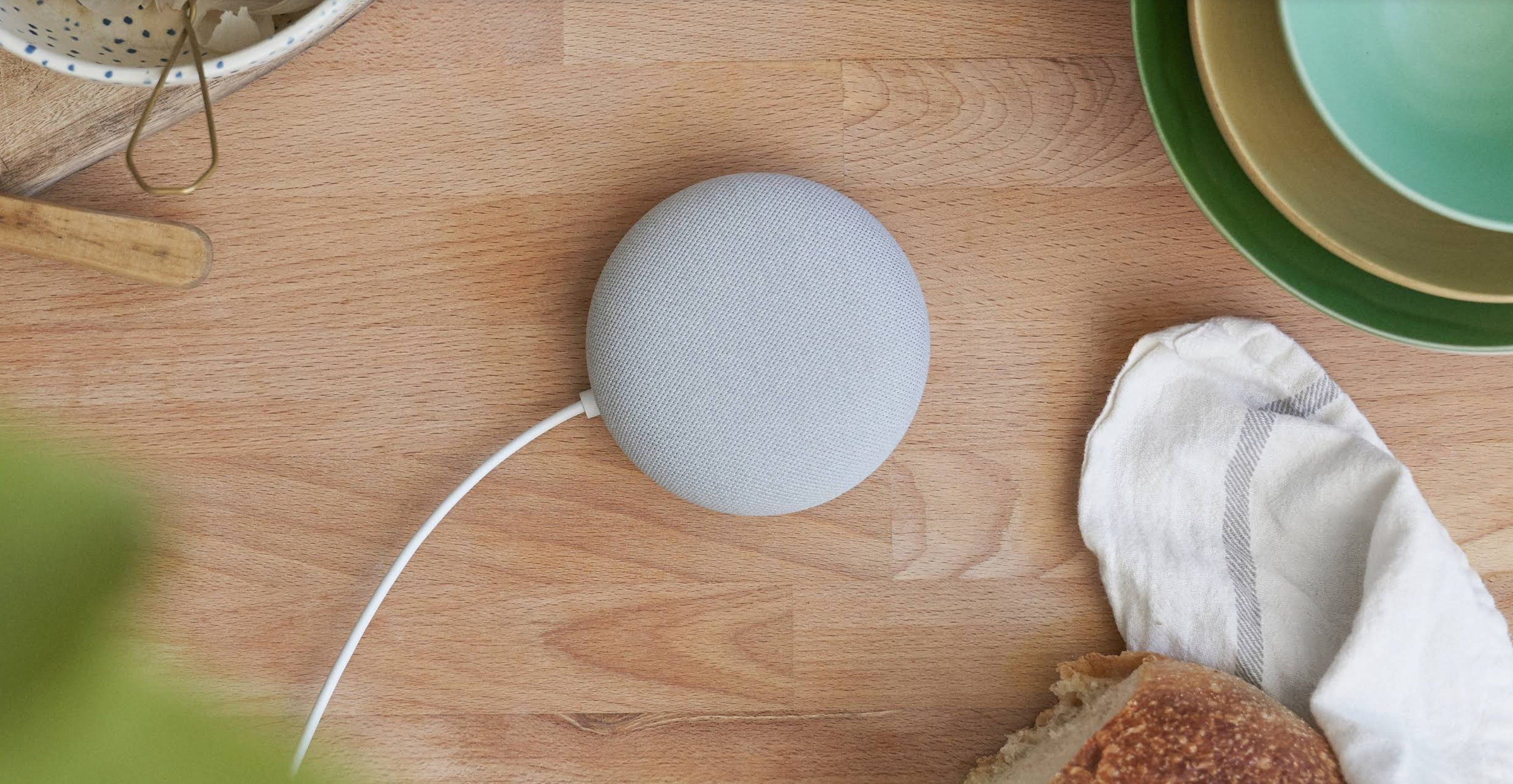 Google Nest Hub Mini on wooden table with various kitchen tools alongside it. 
